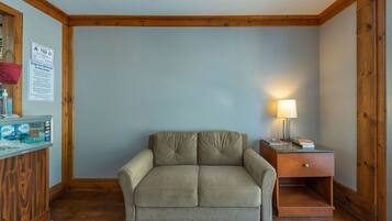 A room with a beige sofa, a wooden desk with a lamp, and a sign indicating dogs are welcome.