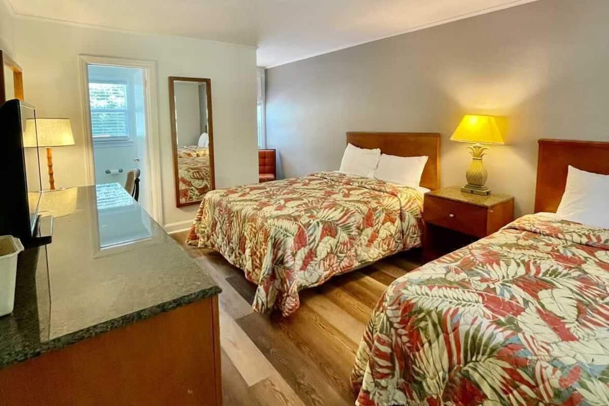 A hotel room with two beds, a desk, and a mirror.