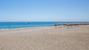 A beach with thatched umbrellas aligned along the shore. - Marina Real apto 211 (Manilva)