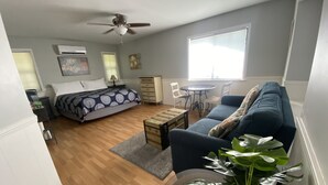 A bedroom with a bed, bedside table, and a ceiling fan. There is a window with blinds, a dresser, and a chair.