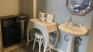 A compact bathroom with a white sink, a small wicker stool, a microwave, and a trash can.