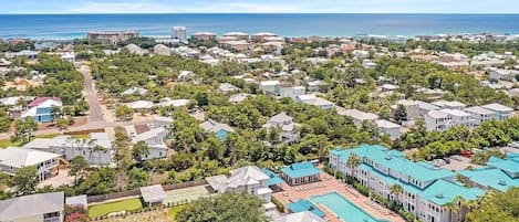 An aerial view of a residential area with houses, a swimming pool, and a view of the ocean.