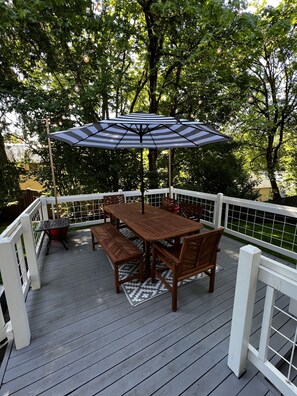 Um deck de madeira com mesa e cadeiras, cercado por um corrimão branco.