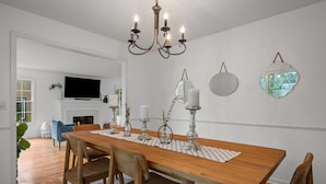 Zona pranzo con tavolo in legno, sedie, un lampadario, candele e decorazioni a parete.