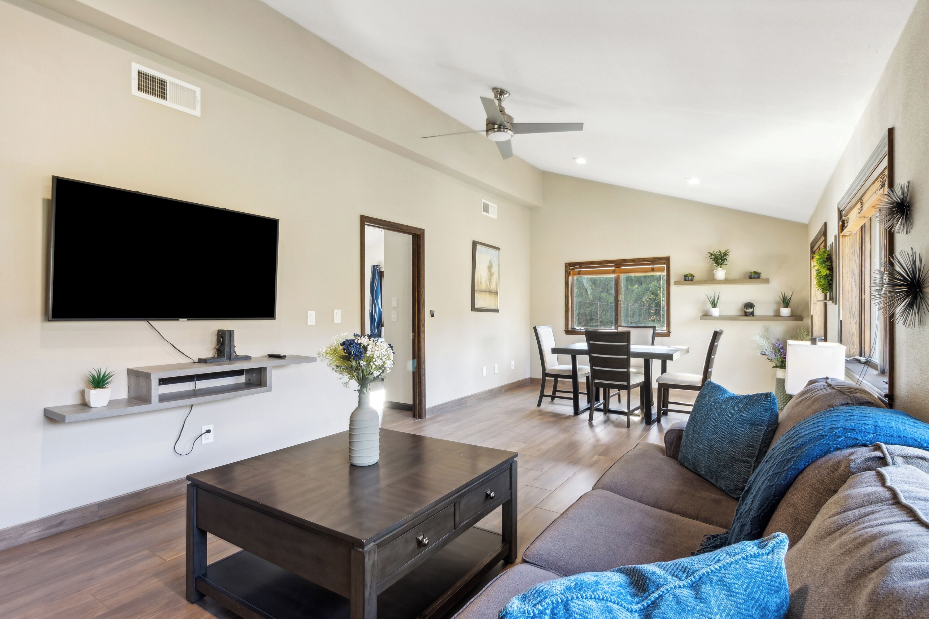 Una sala de estar moderna con un televisor de pantalla plana, una mesa de centro, un sofá y un comedor con sillas y una mesa.
