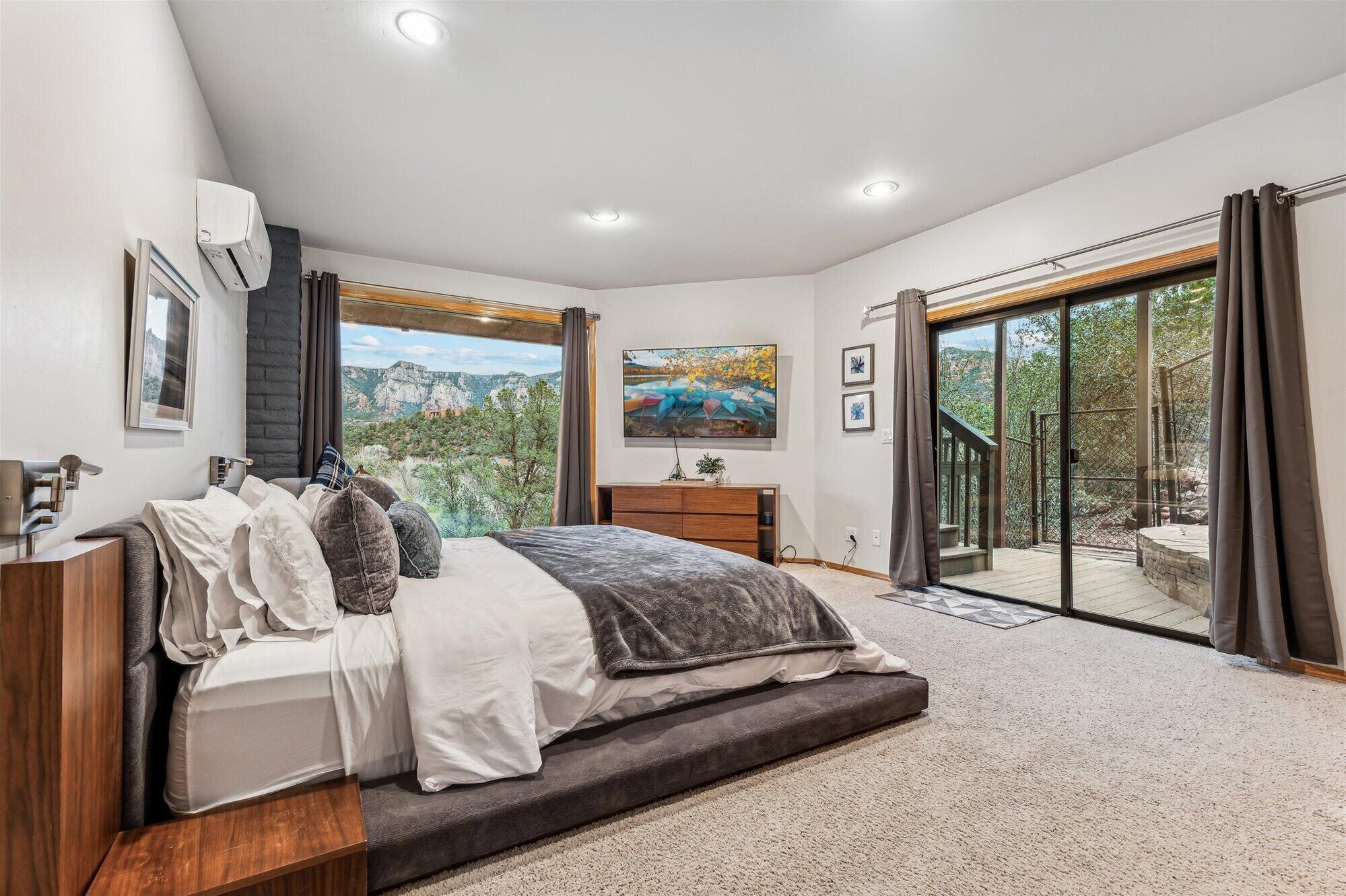 A bedroom with a bed, a TV, a window with a mountain view, and a sliding glass door leading to an outdoor area.