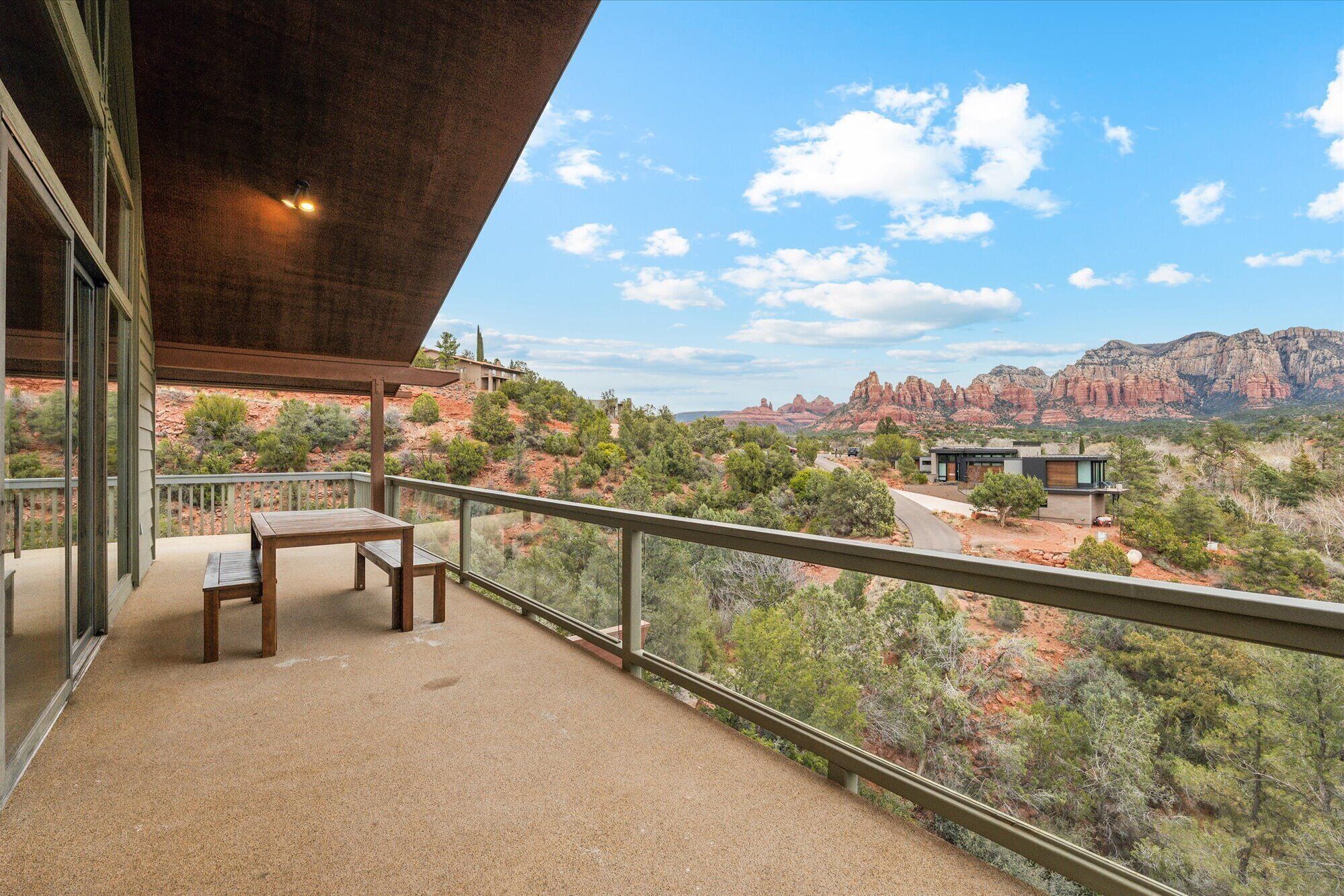 A balcony with a table and chairs, overlooking a desert landscape with red rock formations and greenery.