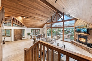 Relax in a spacious interior with a high ceiling, fireplace, and large windows offering panoramic views of the surrounding landscape.