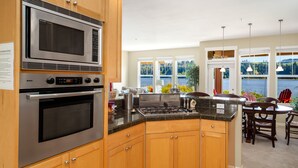 A kitchen with a Bosch microwave, oven, and stove, wooden cabinets, granite countertops, and a view of a lake through large windows. - Happy Place at the Beach (Port Ludlow)