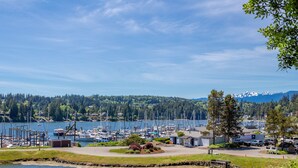 A marina with boats docked, a small building, and a view of a forested area with mountains in the background. - Happy Place at the Beach (Port Ludlow)
