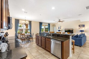 Una cocina moderna con una isla central, un comedor con mesa y sillas, y una sala de estar con sofá y televisor.