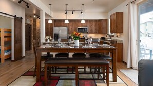 Une cuisine moderne avec des meubles en bois, des appareils en acier inoxydable et un coin repas avec une table dressée pour quatre personnes.