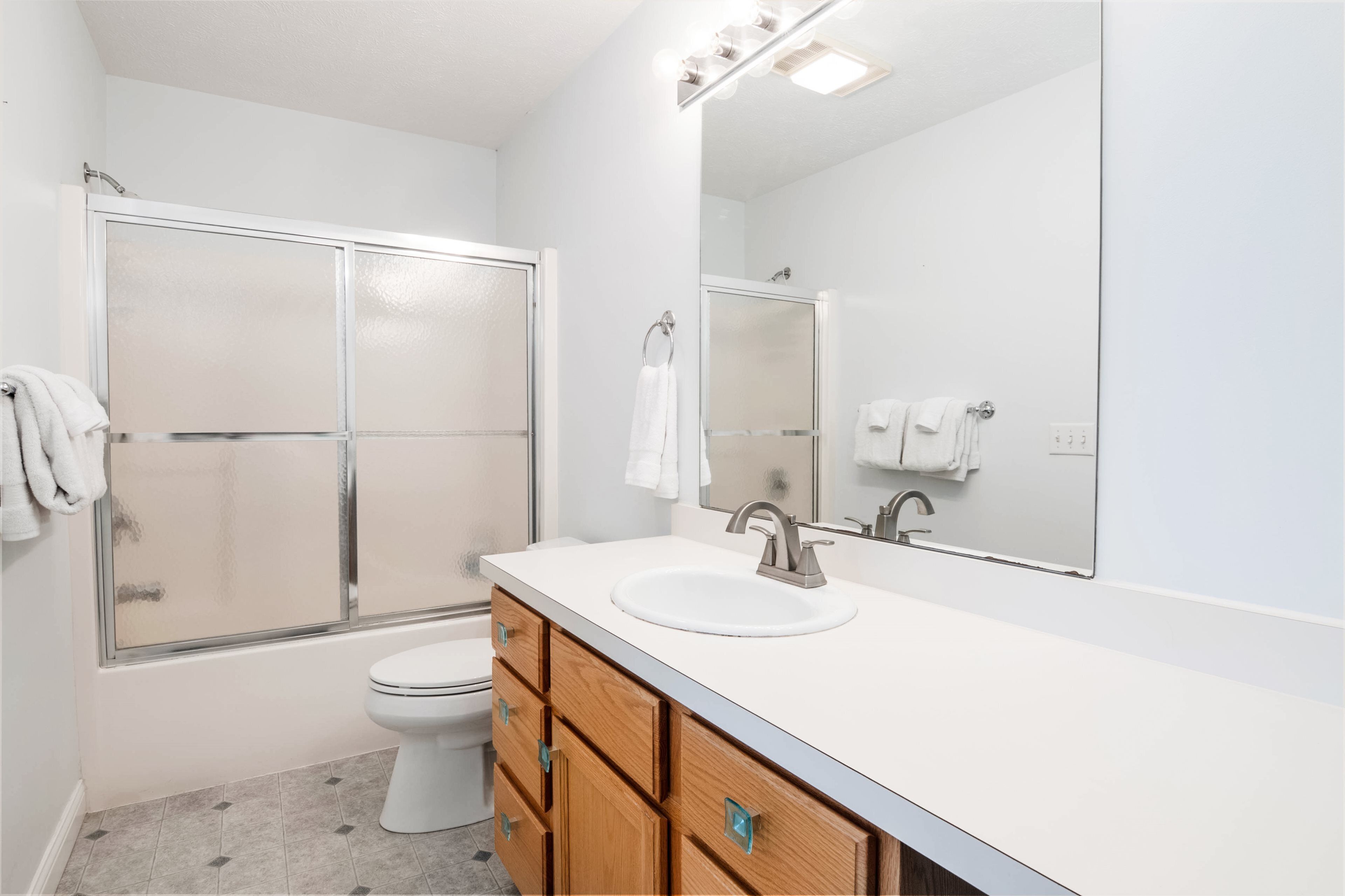 A modern bathroom with a glass-enclosed shower, a white sink, and a large mirror.