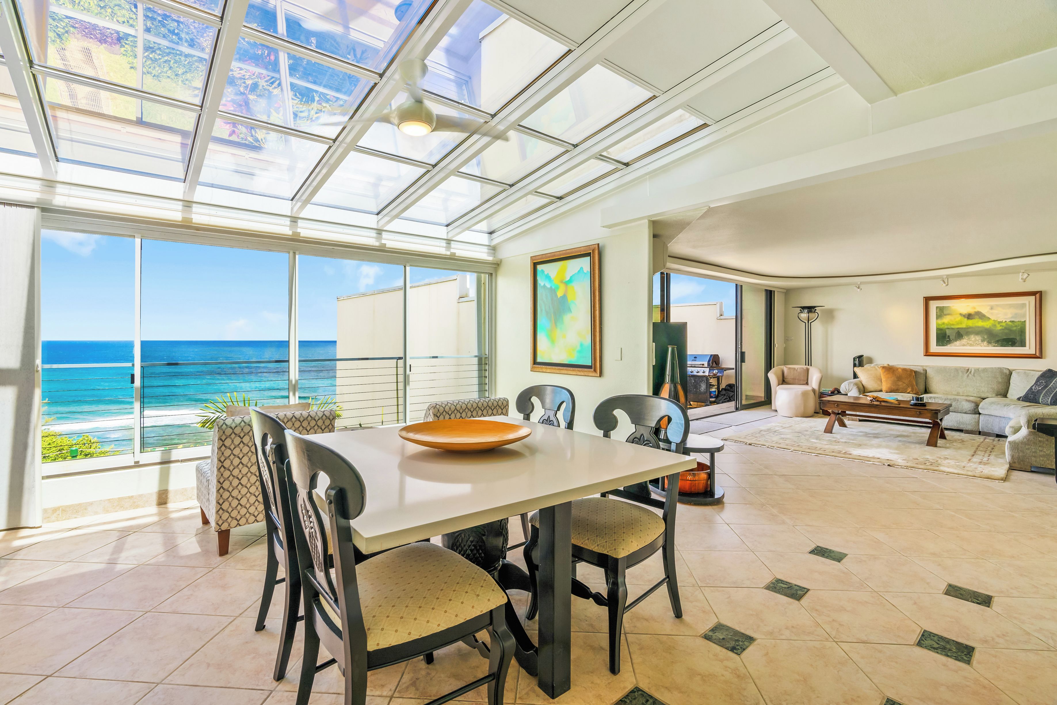 Un vaste espace de vie doté d’une grande baie vitrée donnant sur l’océan, d’une table à manger avec des chaises et d’un coin salon confortable avec un canapé et des fauteuils.