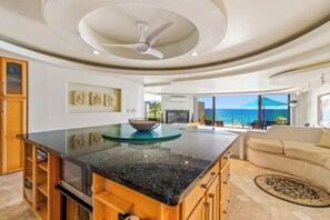 A modern kitchen with a central island, wooden cabinets, and a view of the ocean.