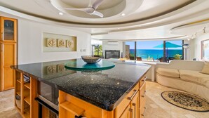 Een moderne keuken met een centraal eiland, houten kastjes en uitzicht op zee.