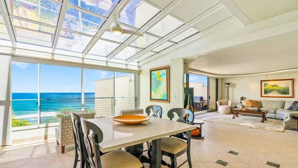 Een ruime woonkamer met een groot raam met uitzicht op de oceaan, een eettafel met stoelen en een gezellige zithoek met een bank en fauteuils.