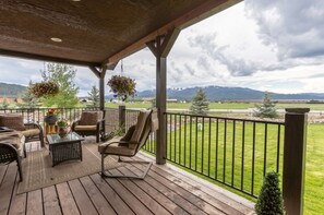 Relax on the covered deck with a sofa, armchairs, and coffee table, surrounded by lush greenery and a serene mountain view.