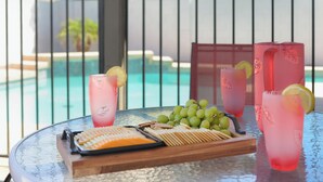 Ein Tisch mit Getränken, Trauben und Snacks auf einem Balkon mit Blick auf einen Pool.