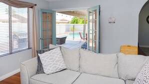 A living room with a sofa, a view of a pool, and a door leading outside. - OCO-Heated pool for additional fee and spacious 4br home for your comfort. (Yuma)