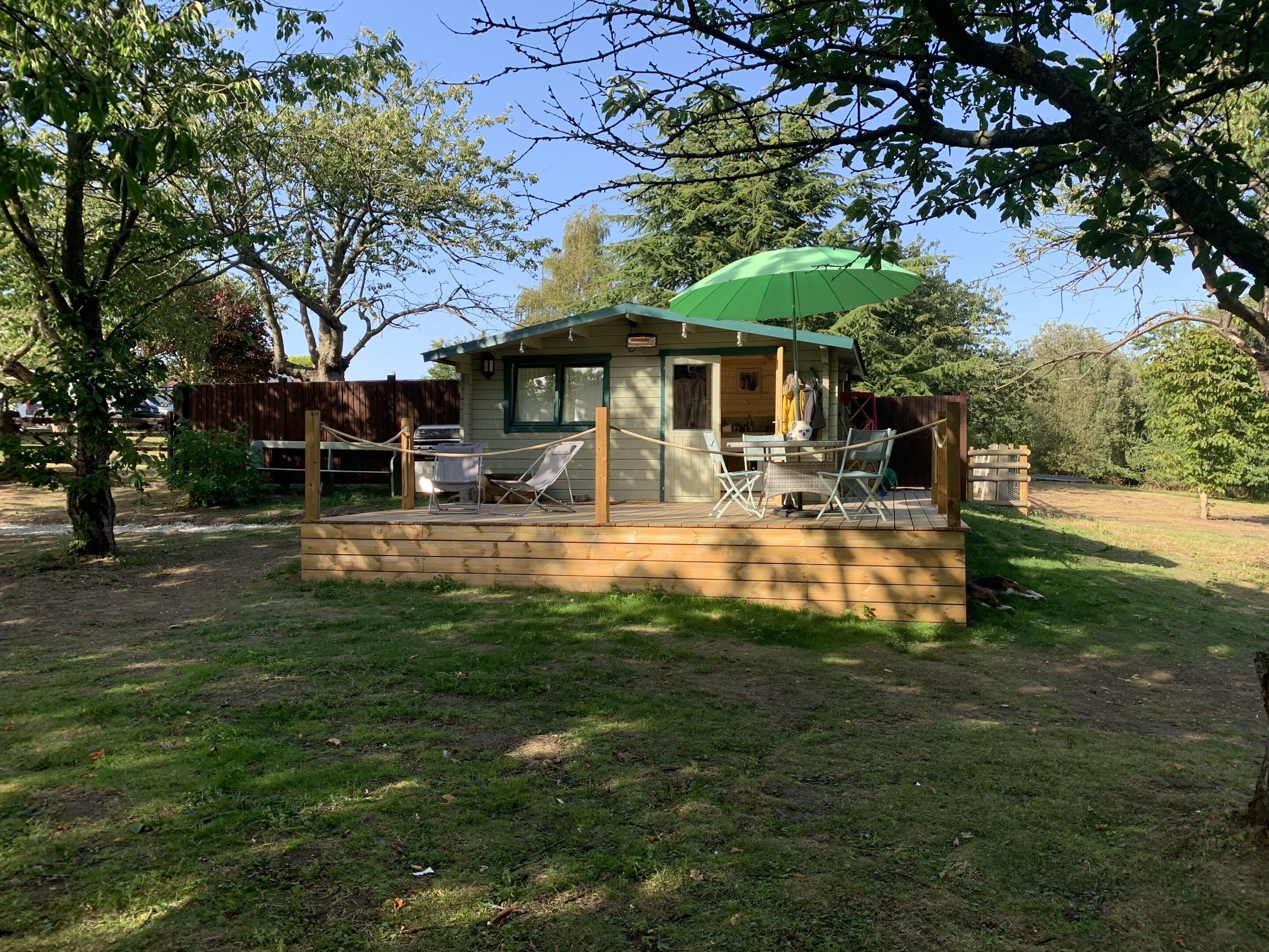 A small wooden cabin with a deck, two lounge chairs, and a green umbrella.