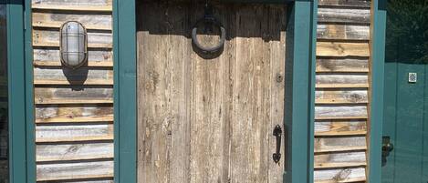 Un bâtiment rustique en bois, avec une porte verte, une plaque portant l’inscription « CHERRY PICKERS » et une petite fenêtre ornée d’une lanterne.