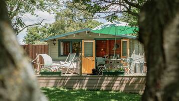 Uma cabana pequena com varanda, área de estar externa e um guarda-sol verde.