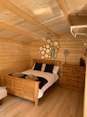 A wooden cabin room with a bed, a dresser, and a wall-mounted mirror. - Truly Kentish Holiday Lets (Sittingbourne)