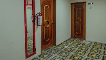 A hallway with patterned flooring, wooden doors, and a fire extinguisher mounted on the wall.