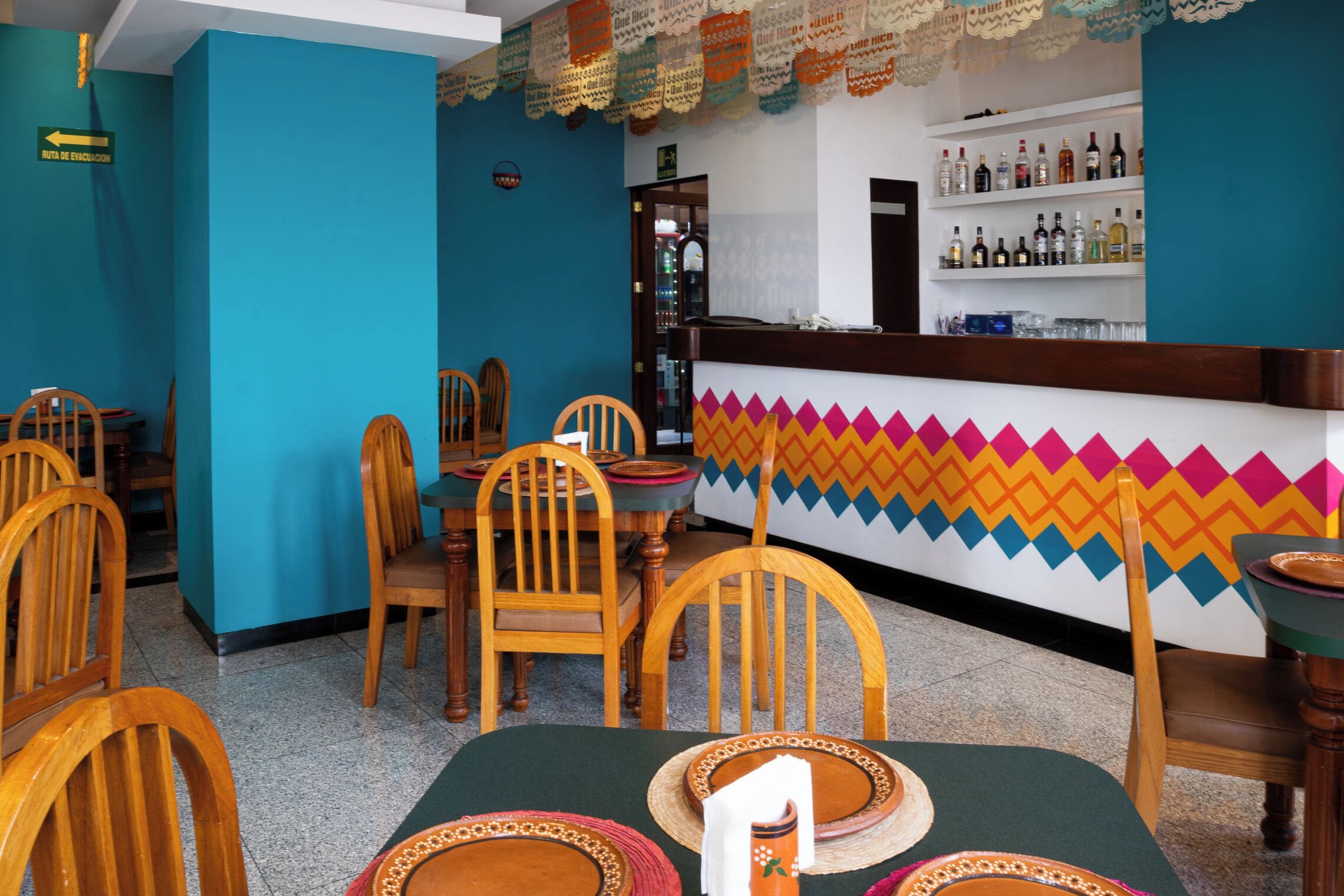 A restaurant interior with wooden chairs, tables, and a colorful wall design.