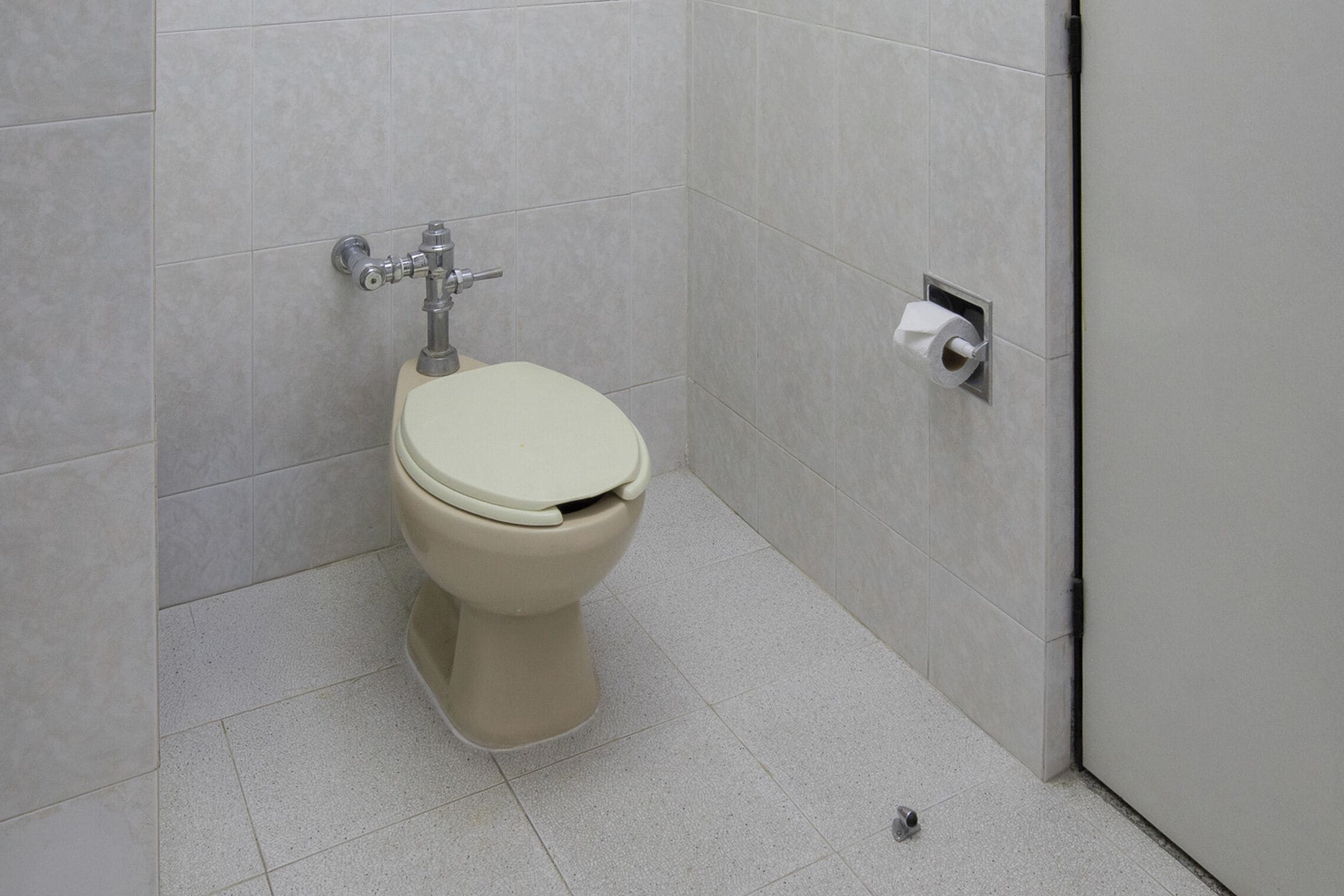 A toilet with a flush handle and a paper towel dispenser in a bathroom with tiled walls and floor.