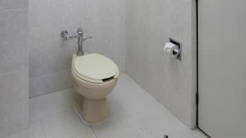 A toilet with a flush handle and a paper towel dispenser in a bathroom with tiled walls and floor.