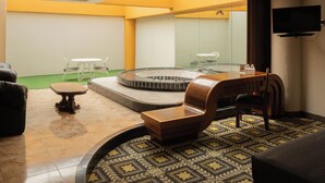 Ein modernes Hotelzimmer mit einer runden Whirlwanne, einem Flachbildfernseher, einem Sofa und einem kleinen Tisch.