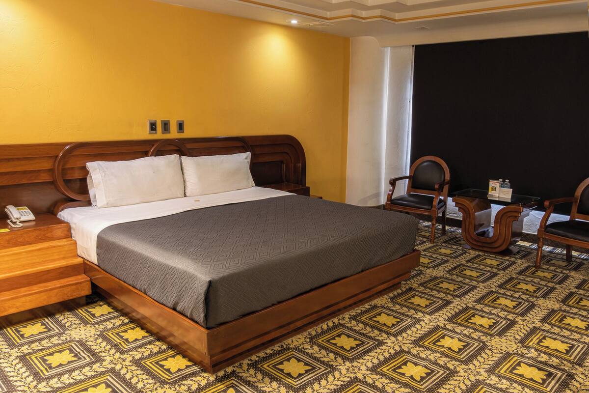 Een hotelkamer met een groot bed, een houten hoofdeinde, een telefoon en een bureau met een stoel.