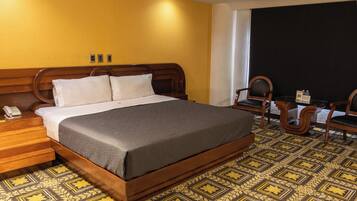 Una habitación de hotel con una cama grande, cabecera de madera, un teléfono y un escritorio con una silla.
