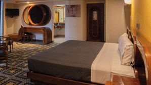 Ein Hotelzimmer mit einem großen Bett, einem Holztisch, einem Stuhl, einem Fernseher und einem Spiegel.