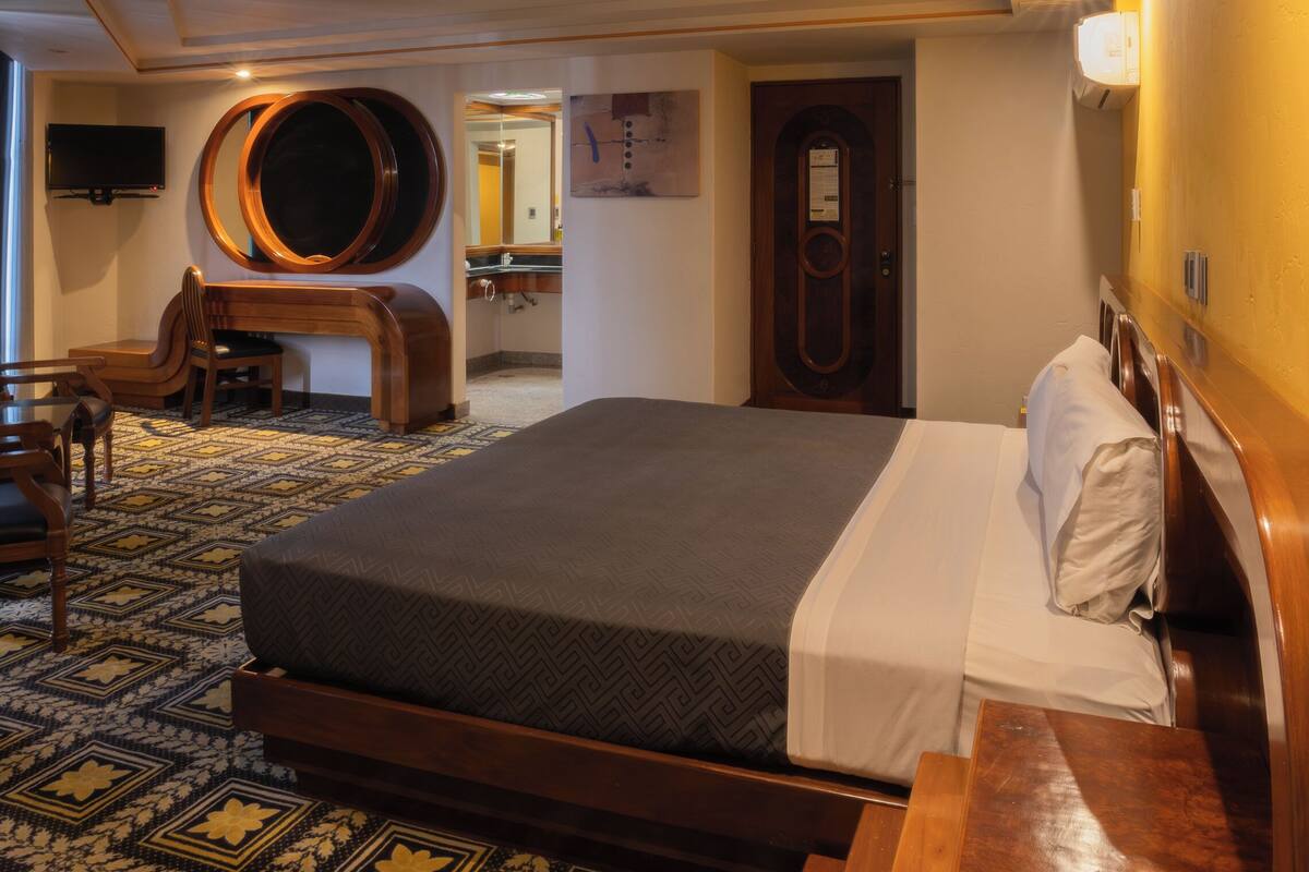 Een hotelkamer met een groot bed, een houten bureau, een stoel, een televisietoestel en een spiegel.