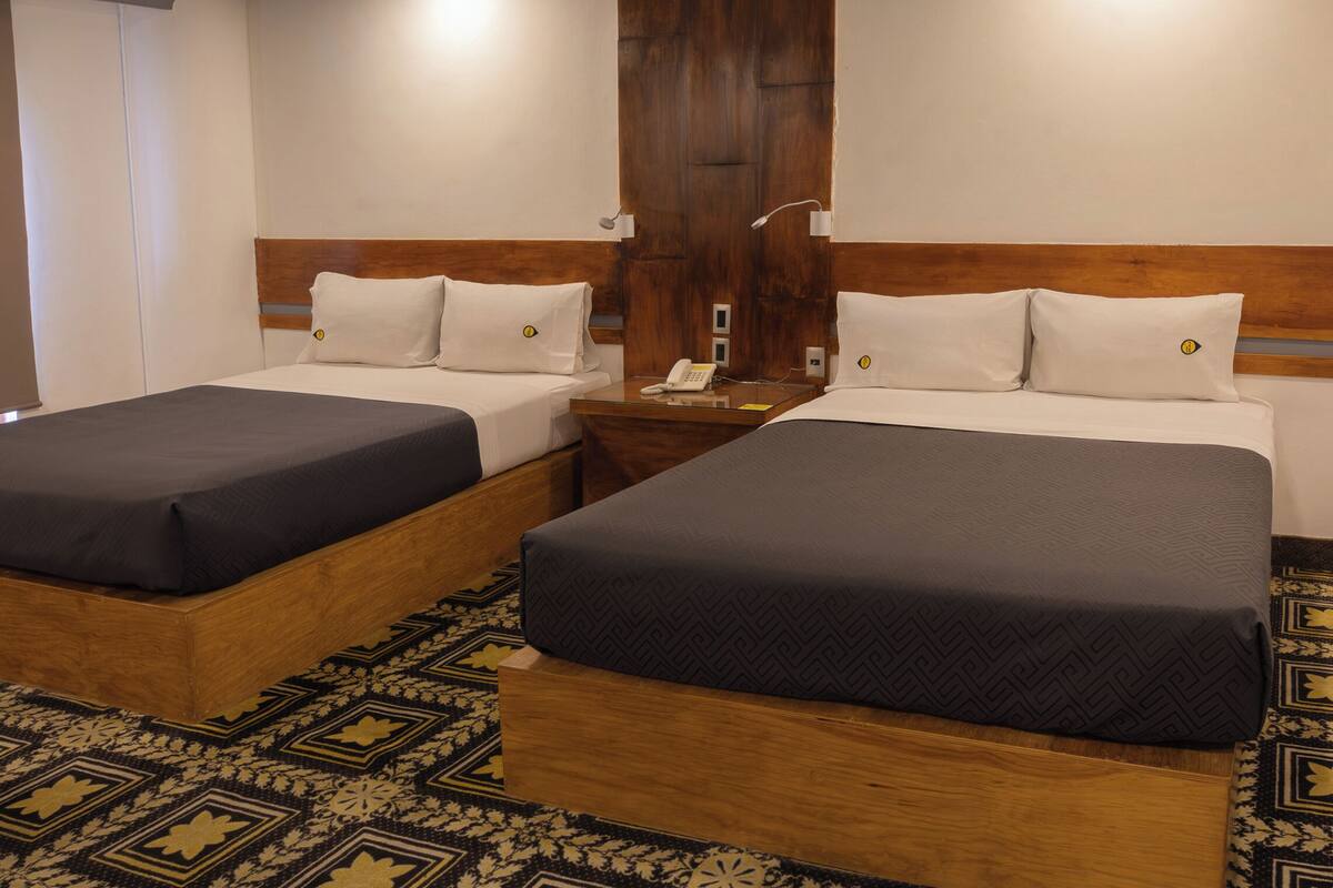 Een hotelkamer met twee bedden, een houten hoofdbord, een nachtkastje met een telefoon en een kamerbreed tapijt met dessin.