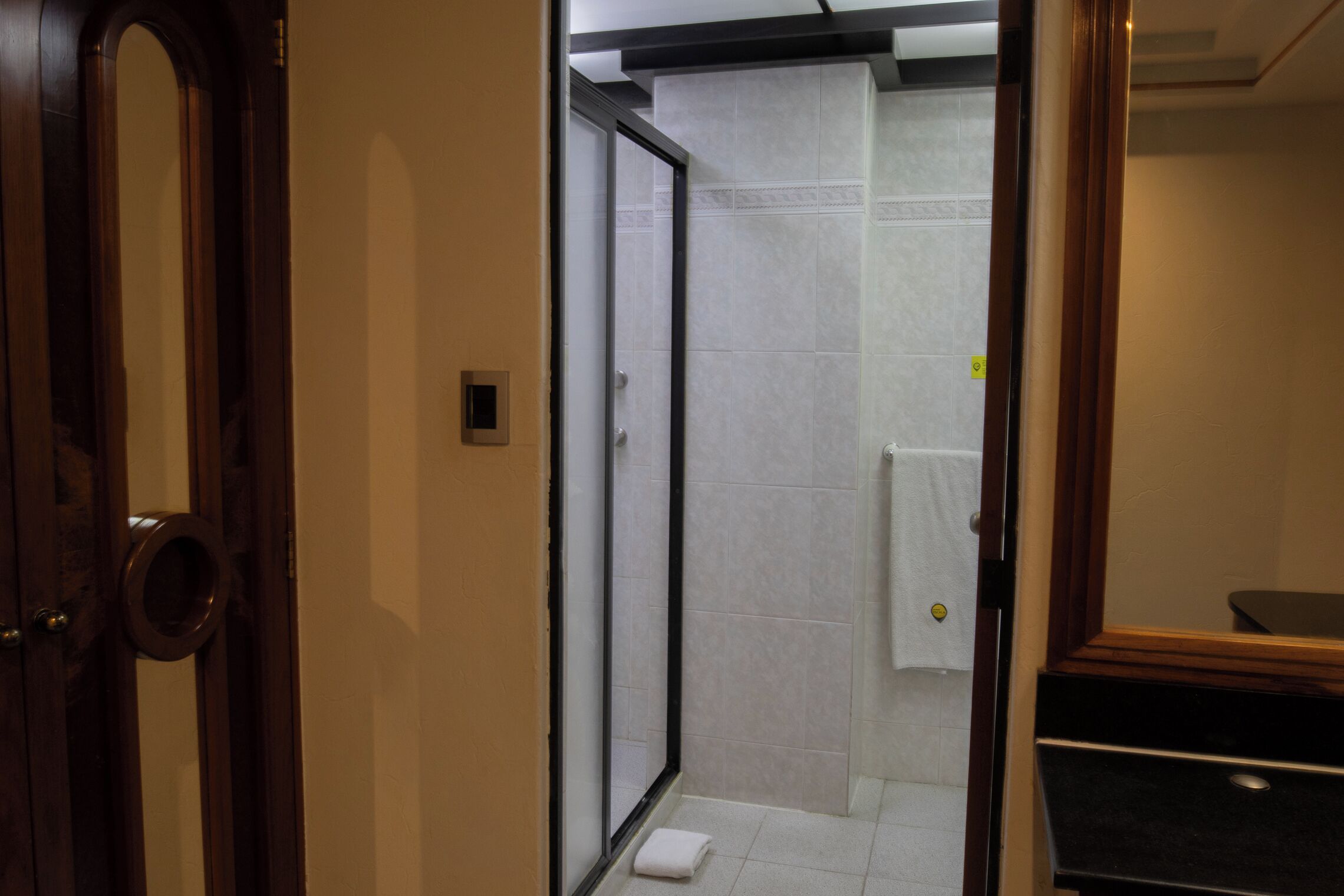 Ein Flur, der zu einem Badezimmer mit Dusche, Toilette und Waschbecken führt.