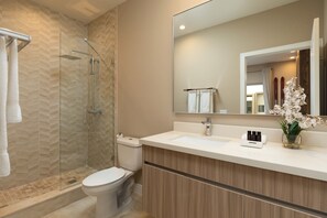Un baño moderno con cabina de ducha de vidrio, inodoro blanco, tocador con espejo y un florero con flores blancas.