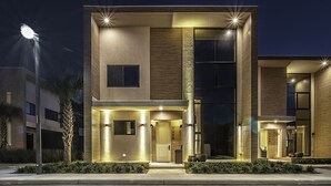 A modern two-story building with a well-lit entrance, large windows, and a visible door number. - Near Disney/Entire Home/Parking/Wi-Fi/Great Lay Out/BBQ Grill/Heated Pool Shared (Kissimmee)