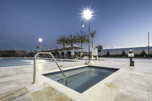 Una piscina con escalera metálica, rodeada de sillones de descanso y sombrillas, con palmeras y cielo despejado al fondo.
