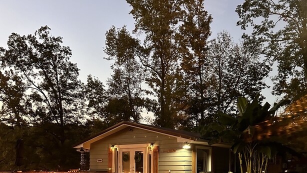 Una casita con porche, un letrero de bienvenida y un jardín iluminado.