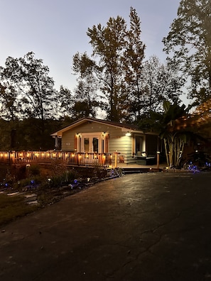 A small house with a porch, a welcome sign, and a garden with lights.