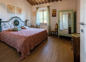 A bedroom with a bed, a chair, a dresser, a window, and a door.