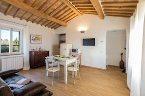 Une pièce avec un plafond en bois, une table à manger avec des chaises, un coin cuisine équipé d’un four à micro-ondes et une fenêtre donnant sur des arbres.