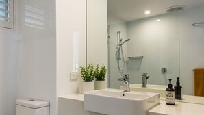 Ein modernes Badezimmer mit einem weißen Waschbecken, einer Handbrause und einem großen Spiegel.