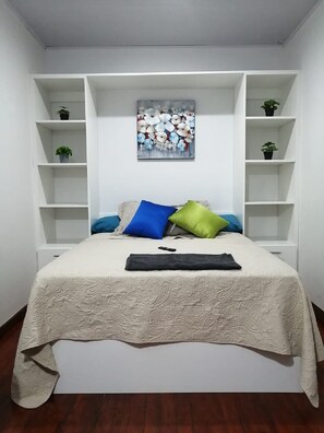 A bedroom with a bed, a painting, and built-in shelving. - Boutique in Heredia (Cerca de Todo - Close to everything) (Heredia)