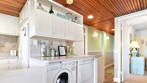 A compact kitchen with a built-in washer and dryer, wooden ceiling, and light green walls.