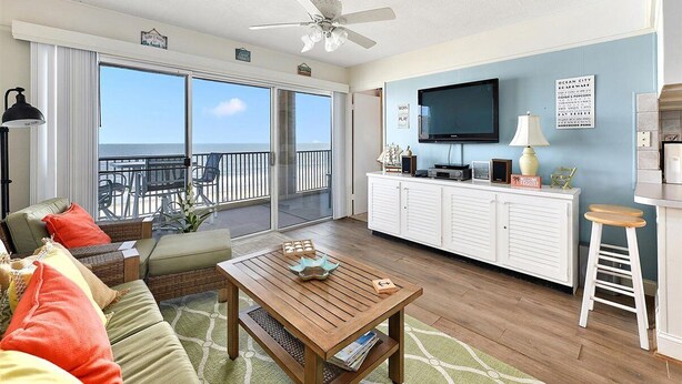 A spacious living area with a balcony, a television, and a kitchen area.